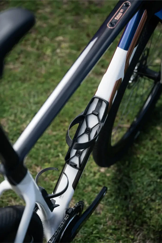 Primer plano de un cuadro de bicicleta BMC Kaius 01 con dos portabidones vacíos montados en el tubo diagonal, colocado sobre hierba, que muestra la esencia de una bicicleta rápida.