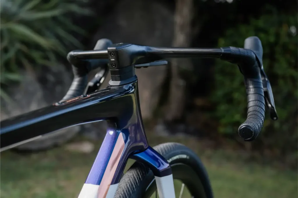 Primer plano del manillar y la potencia integrados de una bicicleta de carretera BMC Kaius 01, mostrando su diseño aerodinámico -perfecto para una bicicleta rápida- con vegetación y rocas difuminadas al fondo.