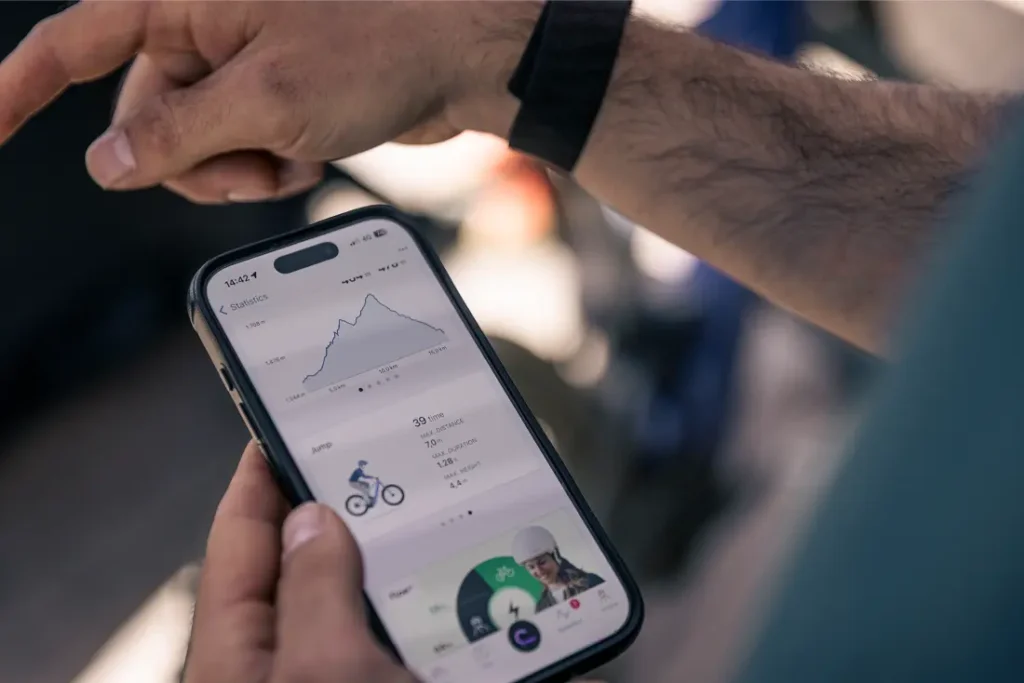 Una persona sostiene un smartphone que muestra una aplicación de seguimiento de la forma física con estadísticas de ciclismo, un gráfico y una imagen de un ciclista, mostrando la actualización Bosch Performance Upgrade para más potencia y mejor experiencia sobre la bici.