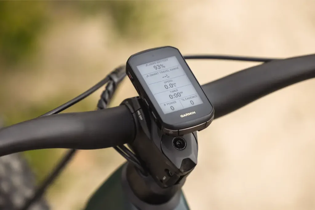 Primer plano de un ciclocomputador Garmin montado en el manillar de una bicicleta, que muestra en su pantalla los datos del recorrido y el estado de la batería: perfecto para los ciclistas que buscan más potencia y una experiencia mejorada sobre la bici.