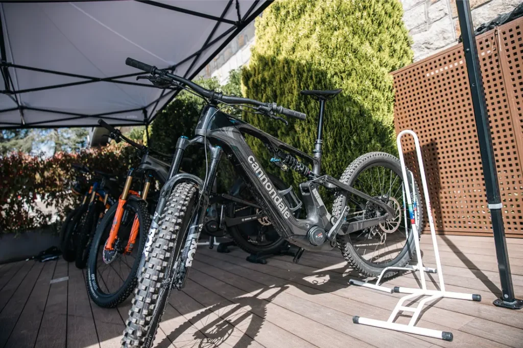Una bicicleta de montaña Cannondale negra está aparcada en una cubierta de madera bajo un toldo, junto a otras bicicletas y un soporte blanco, lista para una actualización Bosch Performance que promete más potencia y una mejor experiencia sobre la bici.