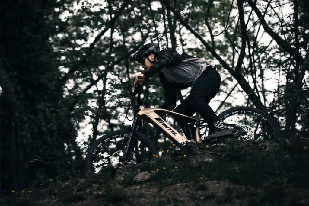 Una persona con casco y equipo de protección conduce una Fantic Sierra e-MTB por un sendero boscoso.