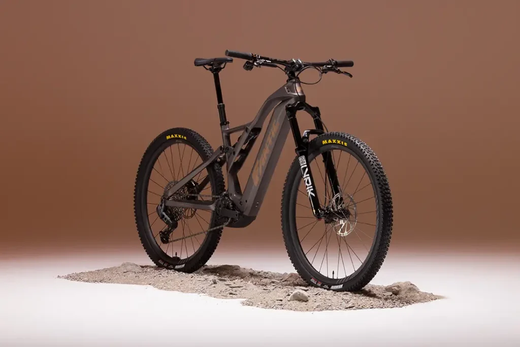 Una Fantic Sierra e-MTB con neumáticos gruesos y suspensión total, propulsada por un motor Bosch CX Gen5, se alza sobre un trozo de tierra sobre un fondo marrón liso.