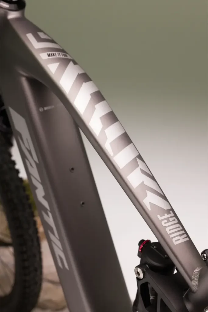 Primer plano de un cuadro de MTB eléctrica gris metalizado con la marca "Santic" y el modelo "Ridge 1.1" en letras blancas.