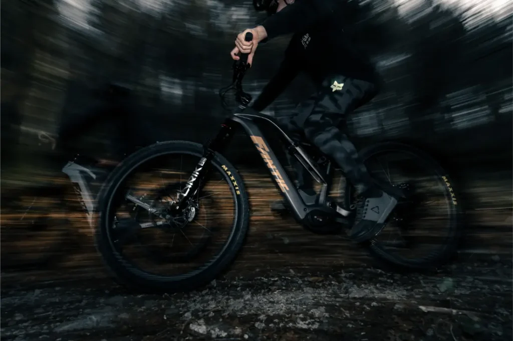 El ciclista atraviesa a toda velocidad un sendero boscoso en una Fantic Sierra e-MTB con suspensión integral, el desenfoque de movimiento resalta el movimiento y el potente motor Bosch CX Gen5 en un entorno oscuro y dinámico.