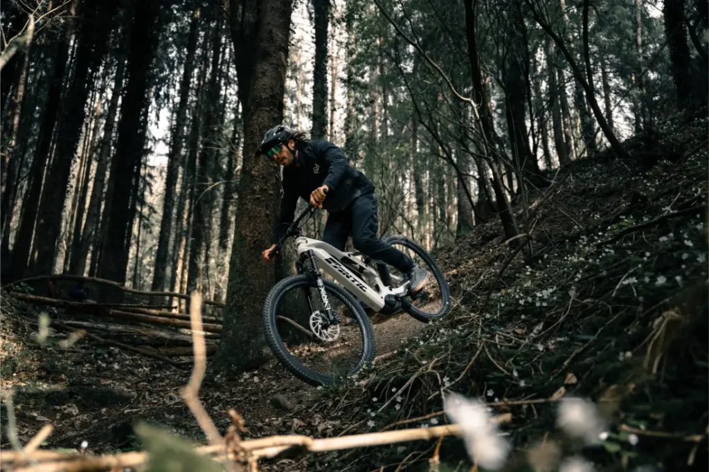 Una persona con casco conduce una Fantic Sierra e-MTB con motor Bosch CX Gen5 por una pista forestal rodeada de árboles y follaje.