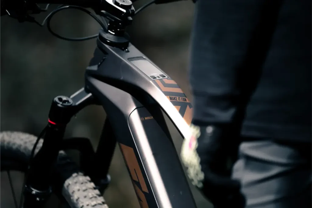 Primer plano del cuadro y la zona del manillar de una Fantic Sierra e-MTB con pantalla digital, que incorpora el motor Bosch CX Gen5, junto a una persona vestida con ropa oscura.