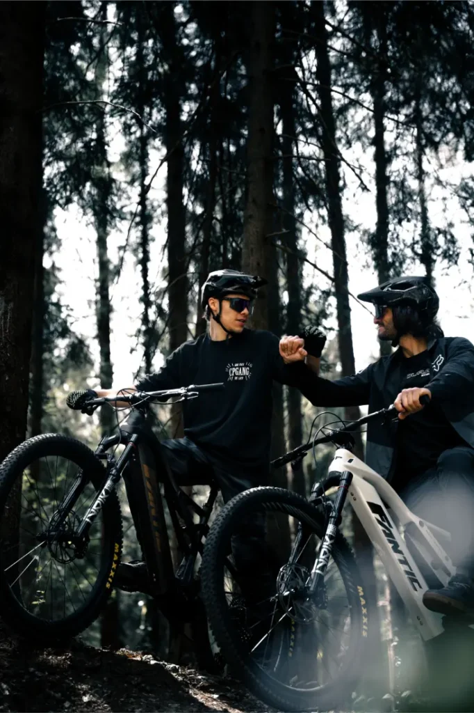 Dos ciclistas con casco y gafas de sol se chocan los puños con sus bicicletas eléctricas Bosch CX Gen5 en un bosque soleado.
