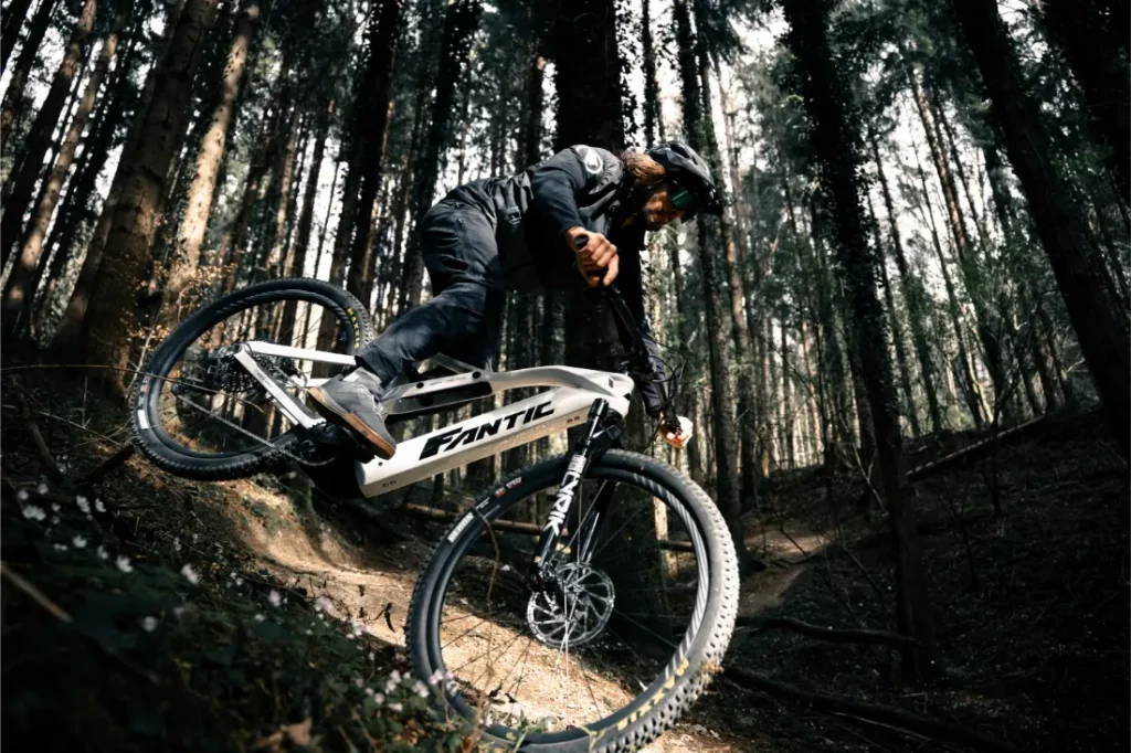 Una persona conduce una Fantic Sierra e-MTB por un sendero de tierra a través de un denso bosque, inclinándose bruscamente mientras toma una curva, propulsada por el motor Bosch CX Gen5.