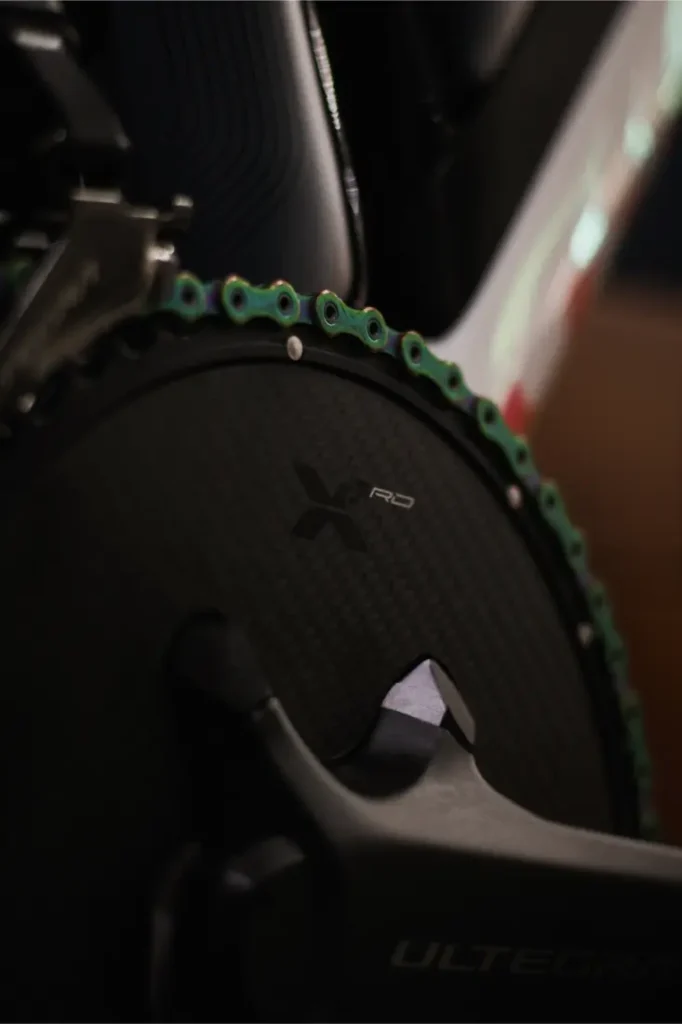 Primer plano de un plato de bicicleta con una cadena KMC X12L Waxed verde Aurora, con la marca "X RD" en el plato y "Ultegra" en el brazo de la biela para una eficiencia silenciosa.