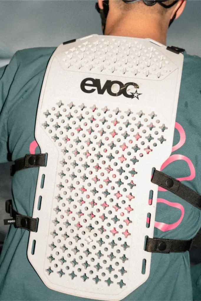 Persona que lleva un EVOC Torso Protector blanco con diseño perforado y correas de sujeción sobre una camiseta verde, aquí en talla XS.