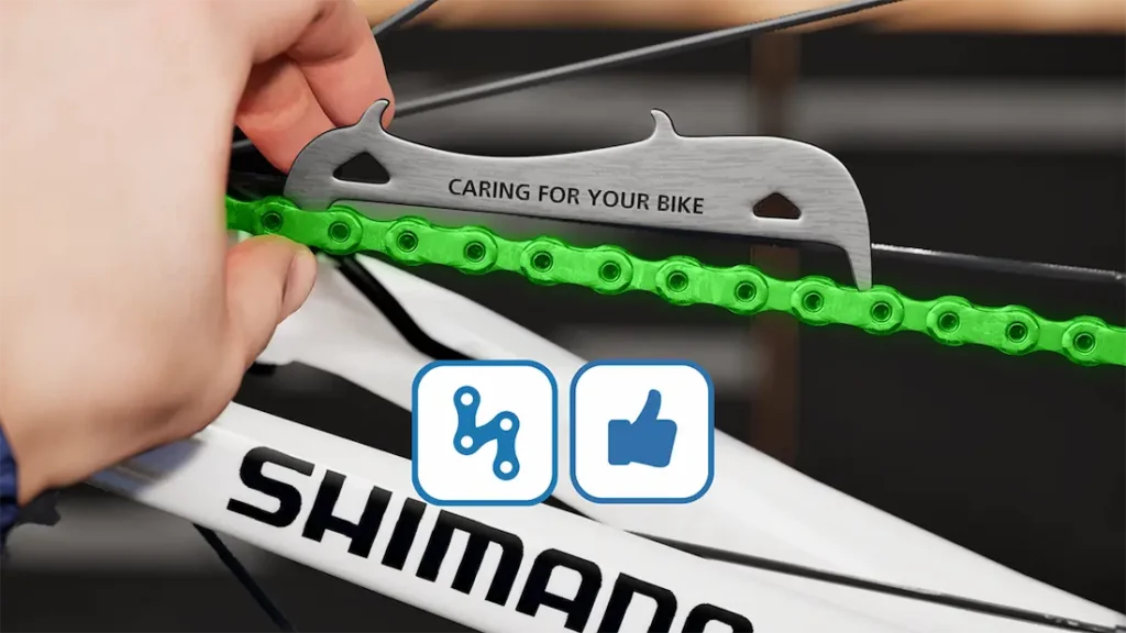 Una mano utiliza un medidor de cadena en una cadena de bicicleta verde, con la palabra "SHIMANO" visible en el cuadro, asegurándose de que la cadena original Shimano se comprueba para ver si está desgastada.