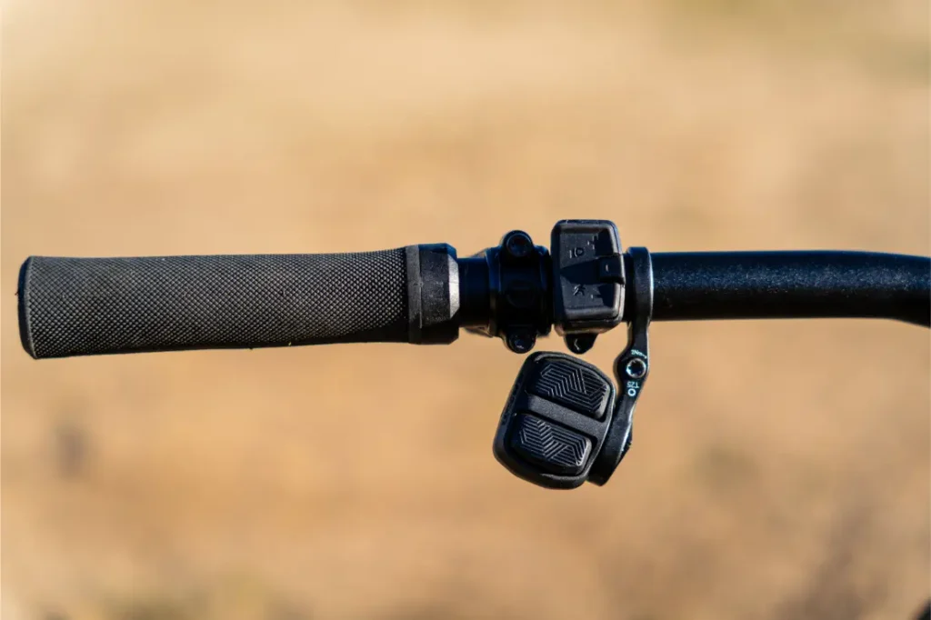 Primer plano de un manillar de bicicleta con empuñadura negra texturizada, botones de control electrónico Bosch de la potente serie Performance Line CX y fondo neutro difuminado.