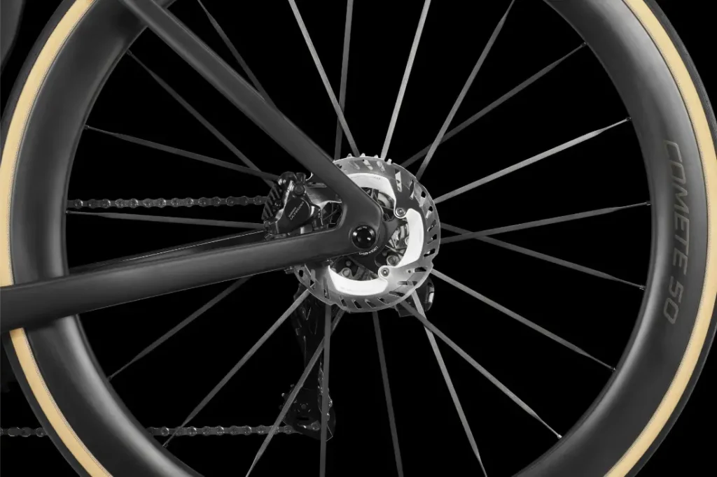 Primer plano de una rueda trasera LOOK 795 Blade RS 3, en la que se aprecian el disco de freno, los radios, la cadena y un neumático con la inscripción «COMETE 50» sobre un fondo negro; fabricada con precisión en Nevers.
