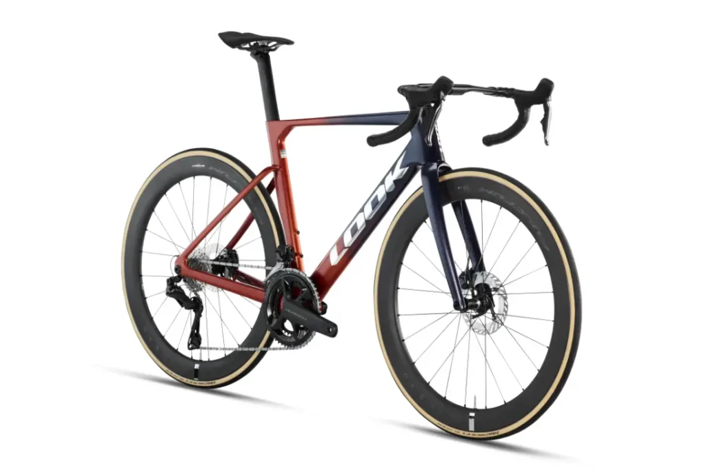 Una bicicleta de carretera con ruedas de perfil alto, manillar de carretera y un cuadro con un degradado de rojo a azul en el que se lee «LOOK» en el tubo diagonal: se trata de la LOOK 795 Blade RS 3, fabricada en Nevers y diseñada para la velocidad.