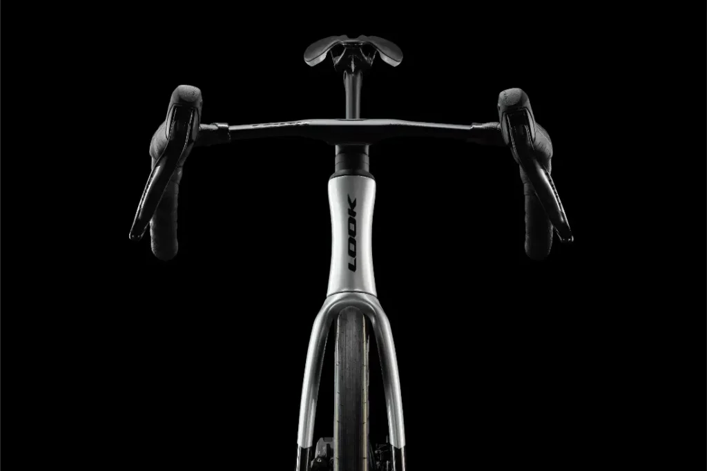 Vista frontal de una moderna bicicleta de carretera LOOK 795 Blade RS 3 con manillar de carretera, sobre un fondo negro. La palabra «LOOK» es visible en el cuadro de la bicicleta, fabricado con precisión en Nevers.