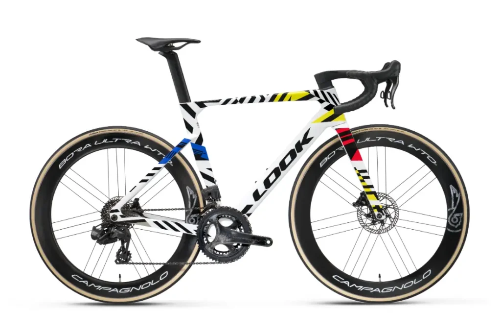 Una bicicleta de carretera LOOK 795 Blade RS 3 con un cuadro en negro, blanco, amarillo, rojo y azul, ruedas de carbono de perfil alto, manillar de carretera y el logotipo «LOOK»: una bicicleta llamativa inspirada en Nevers.