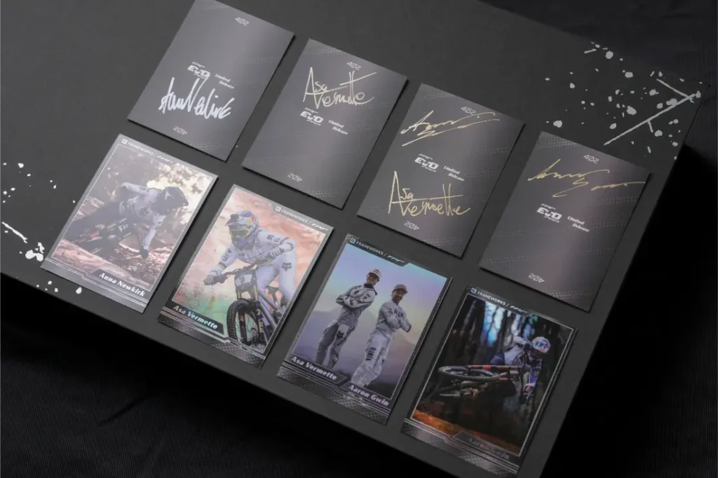 Un conjunto de cromos coleccionables expuestos sobre una superficie negra, con imágenes de ciclistas de montaña y varios cromos TRP EVO PRO Anniversary Edition con firmas doradas, todo ello presentado como una edición limitada inspirada en la Península Ibérica.