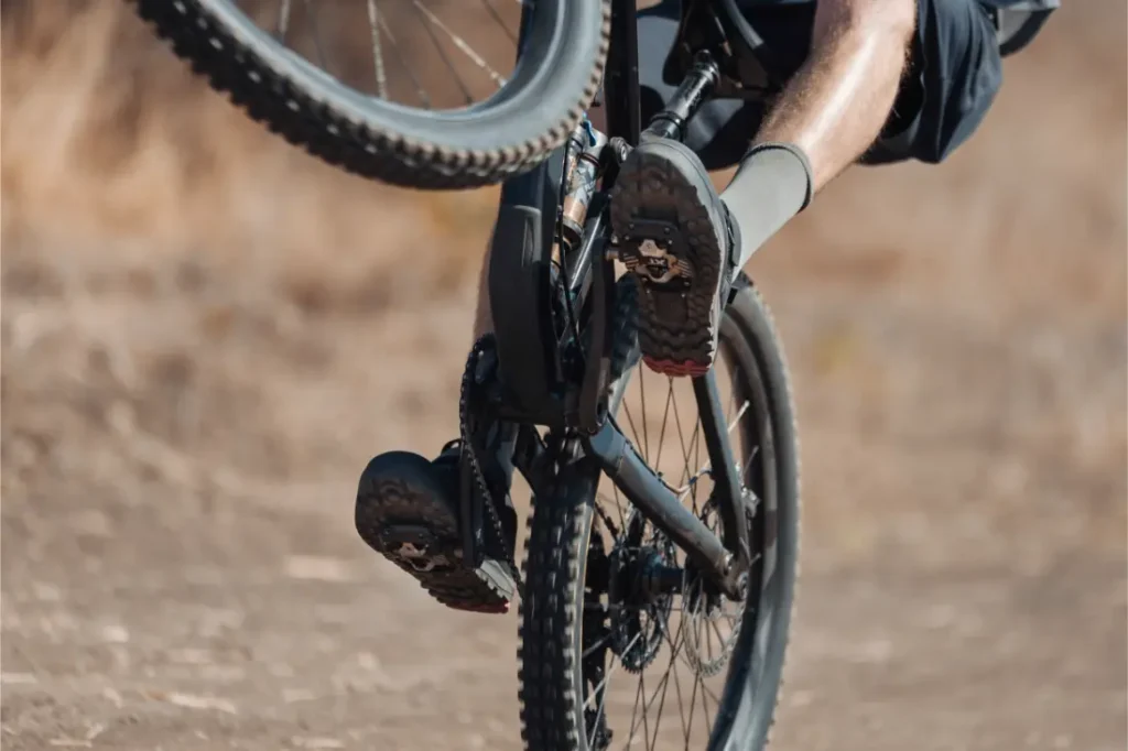 Una persona que va en bicicleta de montaña equipada con pedales Shimano DEORE XT hace un «wheelie» en un camino de tierra, con solo la rueda trasera tocando el suelo.