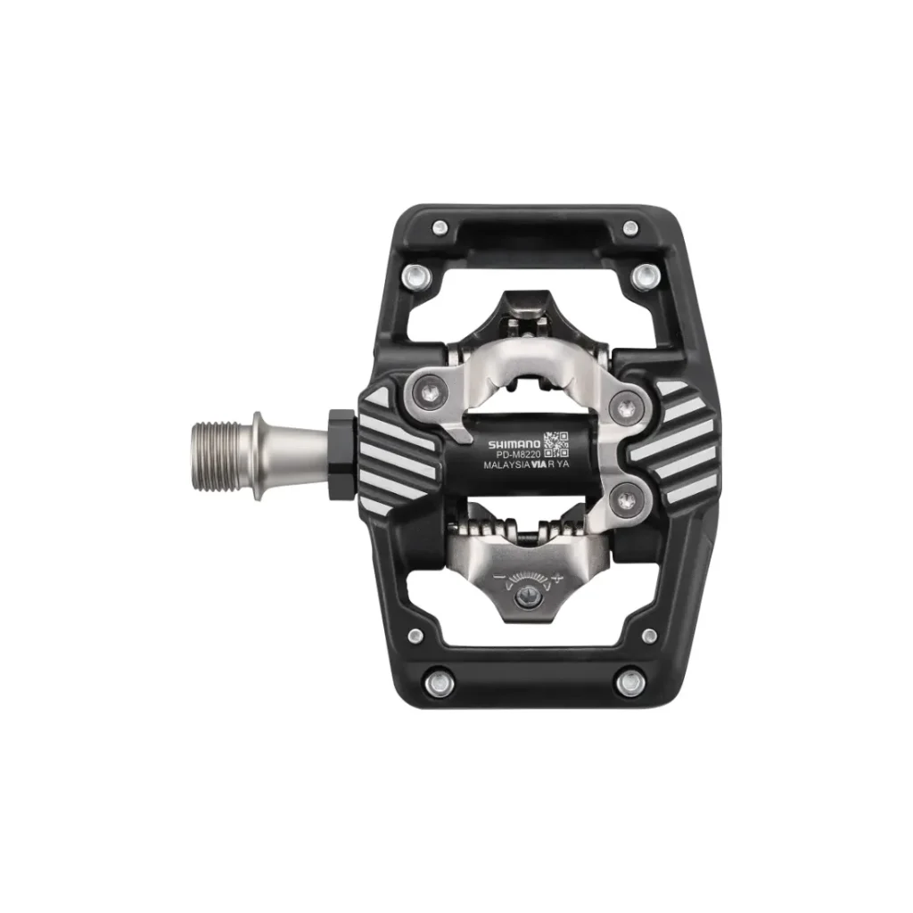 Un pedal de bicicleta Shimano DEORE XT, en negro y plateado, con una estructura rectangular abierta y un eje metálico, diseñado para ofrecer un rendimiento SPD XC Gravel, mostrado sobre un fondo blanco.