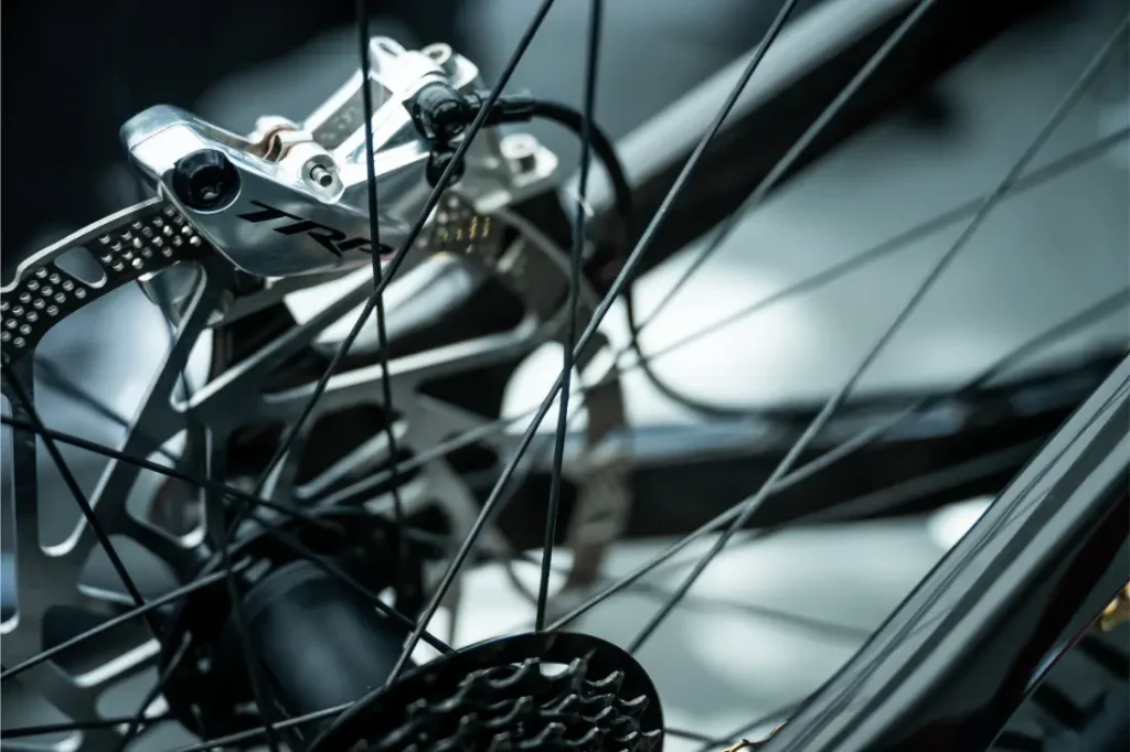 Primer plano de una rueda de bicicleta equipada con el sistema de frenos de disco TRP EVO PRO Anniversary Edition, en el que se aprecian los radios, la pinza de freno y parte del cassette, en una edición limitada exclusiva para la Península Ibérica.