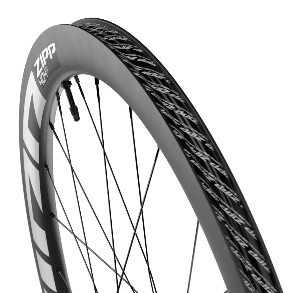 Primer plano de una rueda de bicicleta de carbono Zipp 404 S en el que se aprecian la llanta, los radios y el dibujo de la banda de rodadura de la marca, famosa por su velocidad.