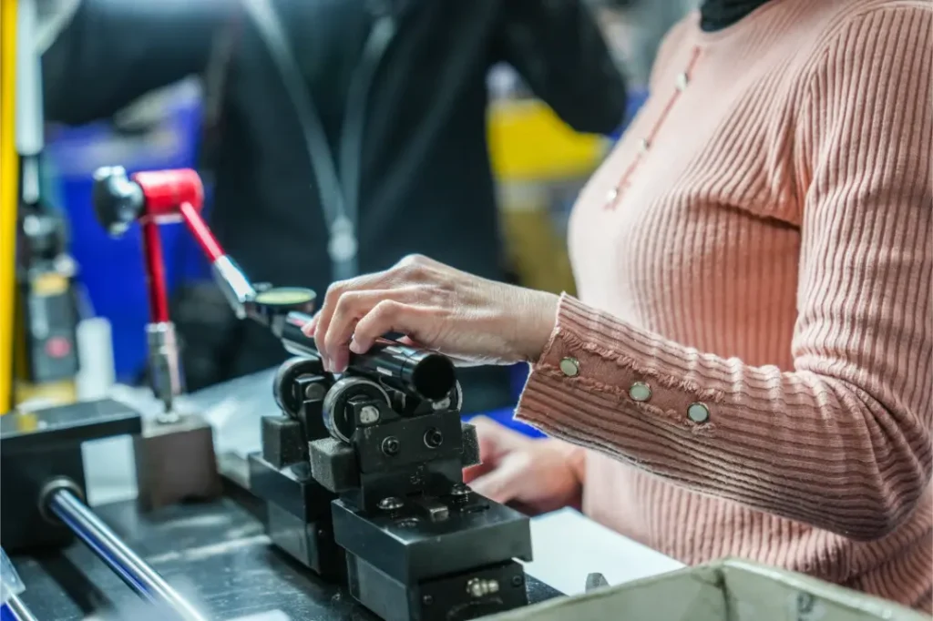 Una persona con jersey rosa maneja una máquina con pinzas metálicas que sujeta un objeto cilíndrico en un entorno industrial, dentro de la distribución oficial de equipos KS Sportmed.