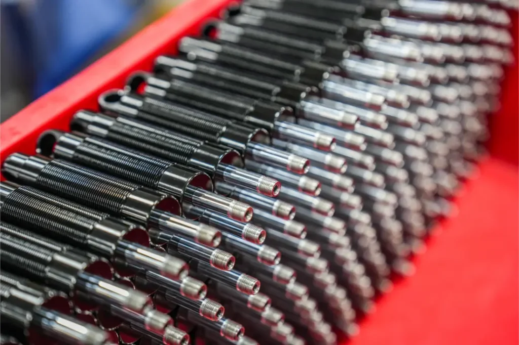 Primer plano de varios muelles metálicos negros con varillas brillantes dispuestos en filas paralelas en un contenedor rojo, parte de un envío de Sportmed distribución KS en España.