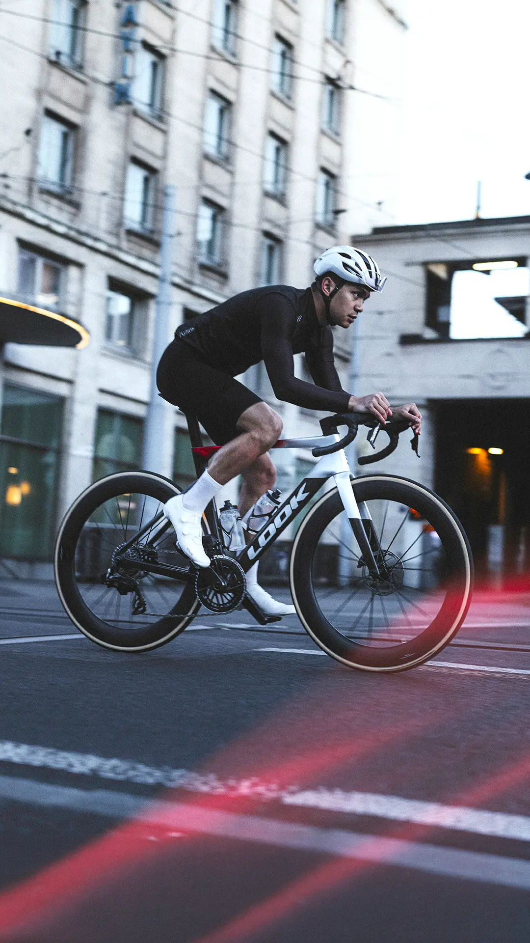 Ciclista vestido de negro que circula en una LOOK 795 Blade RS 3 por una calle de Nevers; lleva casco y calcetines blancos, con luces difuminadas en primer plano.