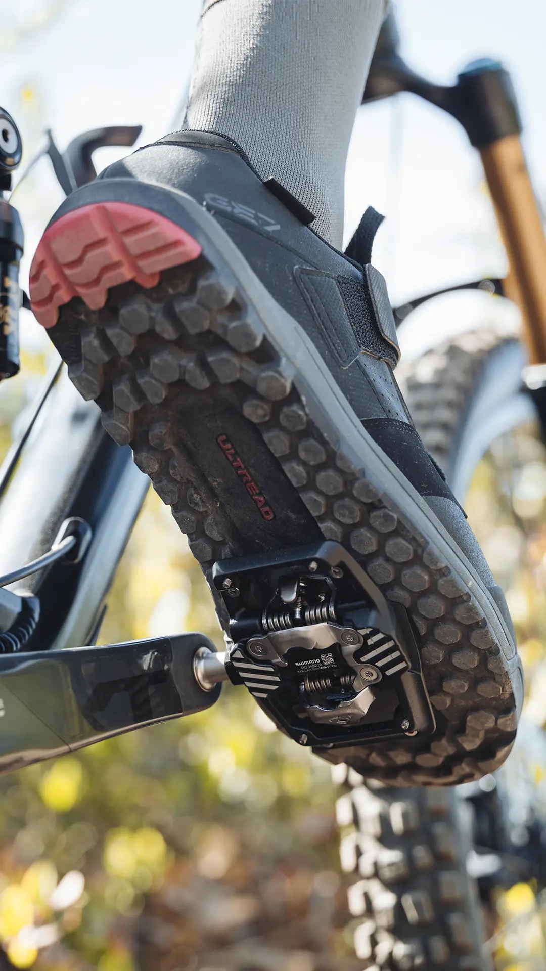 Primer plano de una zapatilla de bicicleta de montaña con suela texturizada acoplada a unos pedales Shimano DEORE XT Trail en una bicicleta.