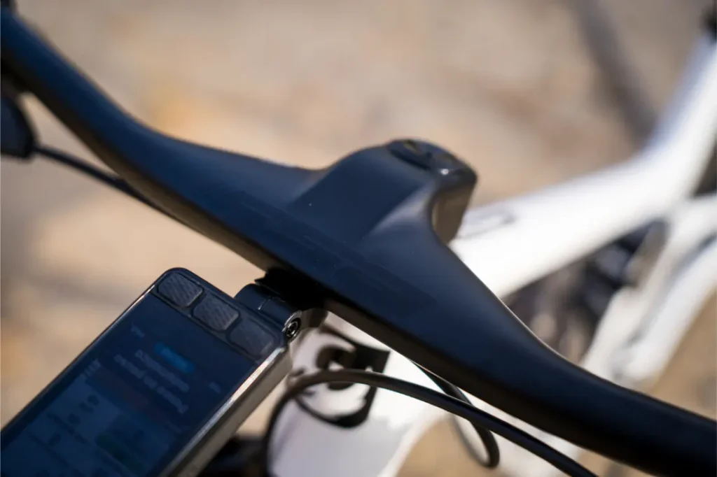 Primer plano del manillar y la potencia de una bicicleta, en el que destaca un manillar integrado de carbono FSA NS SIC, con un dispositivo electrónico acoplado que muestra información, todo ello montado en un cuadro blanco de bicicleta de montaña.