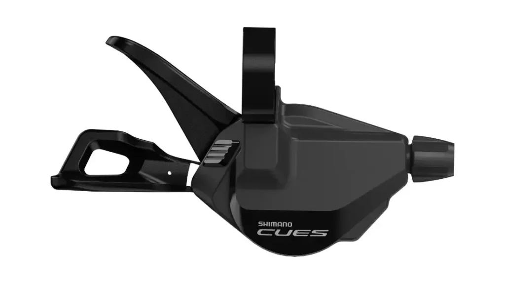 Una palanca de cambio de bicicleta Shimano CUES de color negro, con dos manetas y el logotipo visible, representada sobre un fondo blanco.