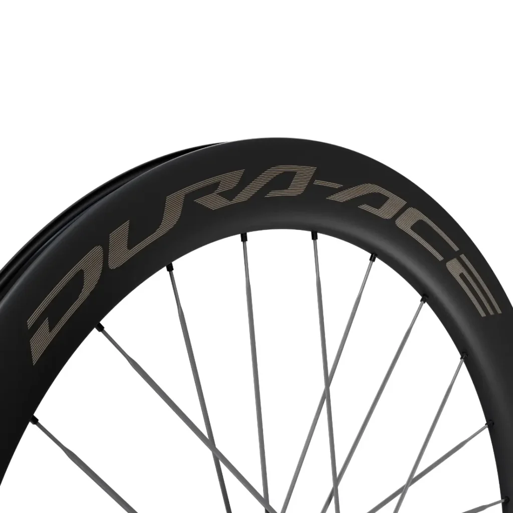 Primer plano de una rueda de bicicleta con llanta negra y la marca «DURA-ACE» en letras grandes, con radios plateados sobre un fondo blanco. Este modelo Shimano Dura-Ace WH-R9370 destaca por sus ruedas de carbono de alto rendimiento, diseñadas para ofrecer velocidad y precisión.