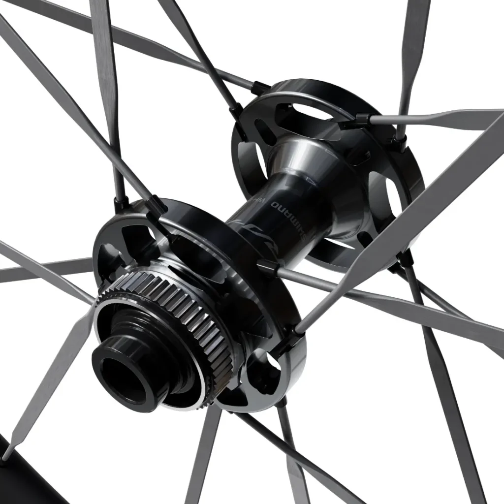 Primer plano del buje de una rueda de bicicleta con radios metálicos que se extienden radialmente hacia fuera, en el que se aprecian con detalle las piezas mecánicas y el logotipo «Shimano Dura-Ace WH-R9370» en el buje central, lo que pone de relieve la ingeniería de precisión que suele caracterizar a las ruedas de carbono.