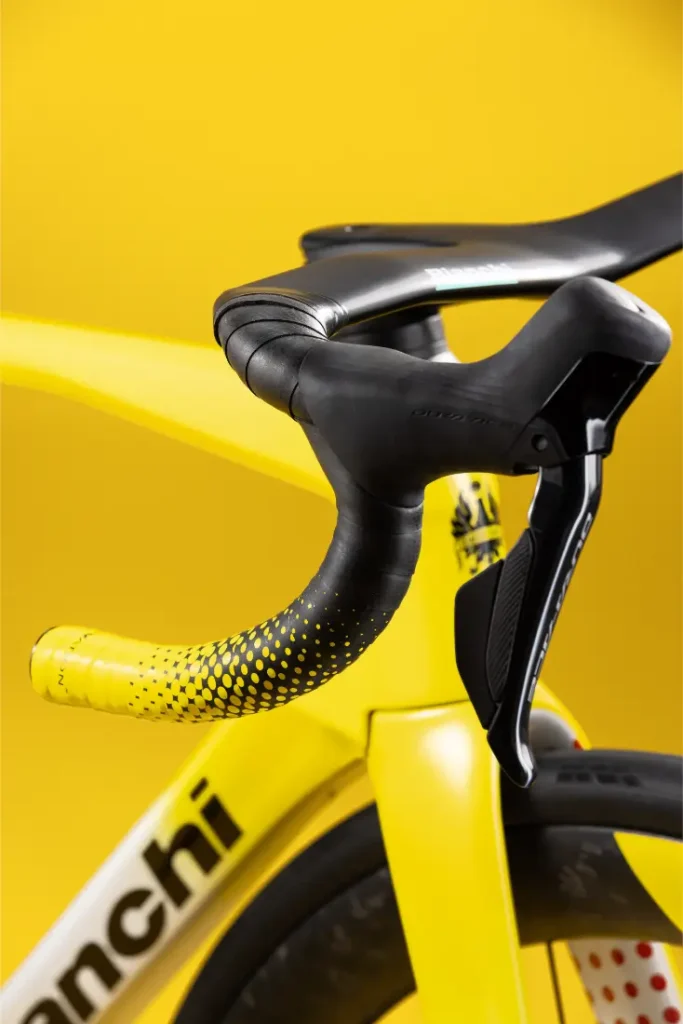 Primer plano del manillar y la palanca de freno de una bicicleta amarilla sobre un fondo amarillo a juego. El cuadro de la bicicleta lleva el nombre de la marca «Bianchi».