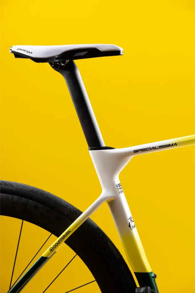 Primer plano del sillín, la tija del sillín y la rueda trasera de una bicicleta de carretera moderna sobre un fondo amarillo brillante.