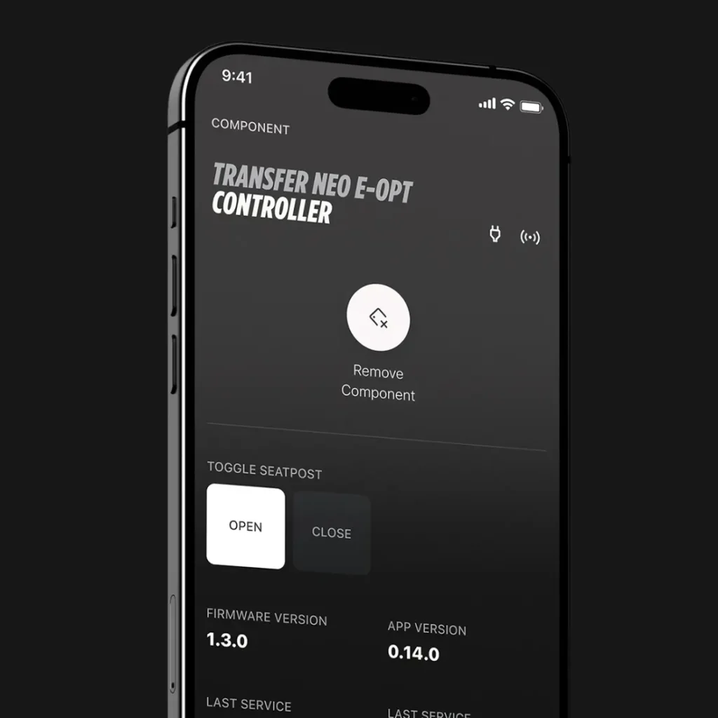La pantalla de un smartphone muestra la interfaz de una aplicación para gestionar un controlador FOX Transfer Neo E-Opt, que incluye opciones para retirar un componente y activar o desactivar la tija de sillín electrónica, además de información sobre el firmware e-Optimized y la versión de la aplicación.