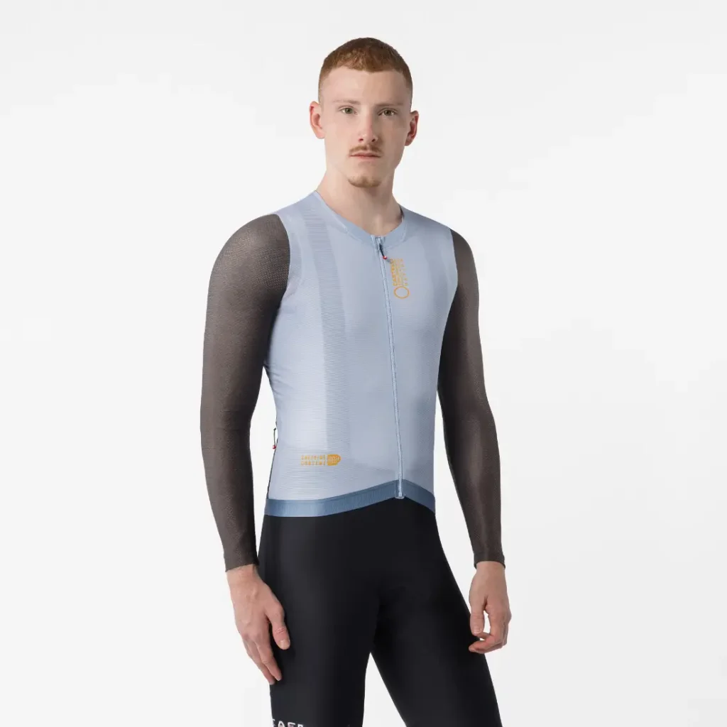 Una persona que lleva un maillot de ciclismo Corretto LS de color azul claro, de manga larga, y unos pantalones cortos negros, de pie sobre un fondo blanco liso.