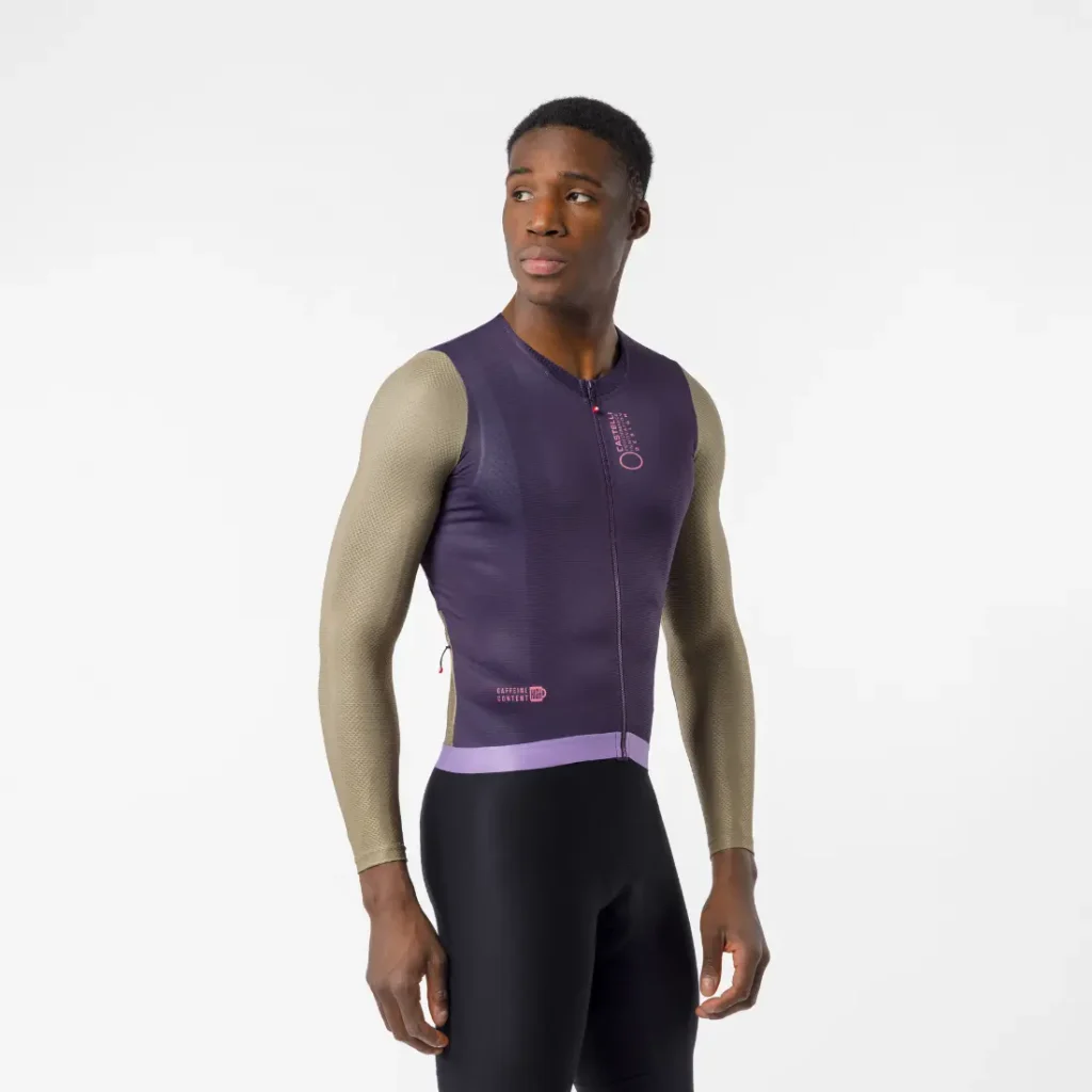 Hombre que lleva un maillot de ciclismo morado sin mangas, que recuerda al modelo «Transition» de Castelli, combinado con mangas largas de color beige y pantalones cortos negros, de pie sobre un fondo blanco liso.