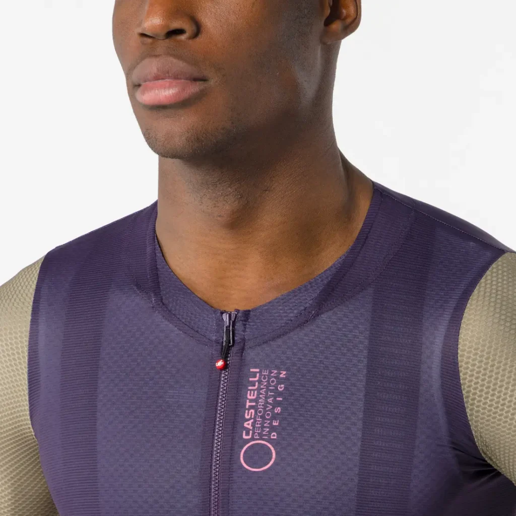 Una persona que lleva un maillot Castelli Corretto LS de manga larga de color morado, con cremallera frontal y mangas grises, fotografiada desde los hombros hacia arriba sobre un fondo liso.