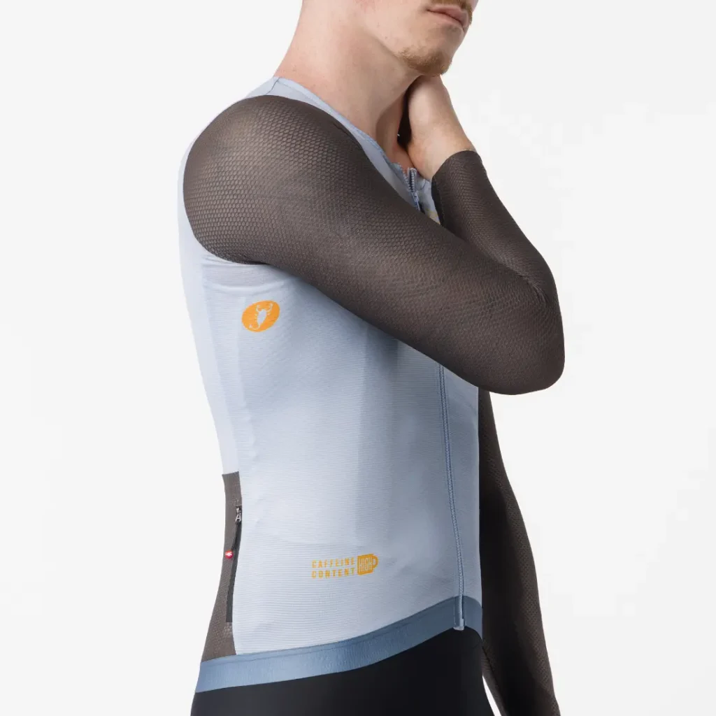 Una persona que lleva un maillot de ciclismo sin mangas Castelli Transition de color azul claro con mangas de malla negras, de pie sobre un fondo blanco liso.