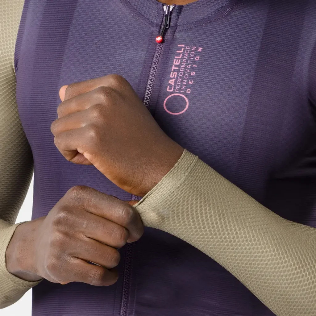 Una persona que lleva un maillot Corretto LS con textura y cremallera se ajusta la manga. El maillot de manga larga es de color morado con la manga en beige y luce el logotipo y el texto de Castelli en el pecho, lo que evoca la comodidad y el diseño aerodinámico de la colección Castelli Transition.