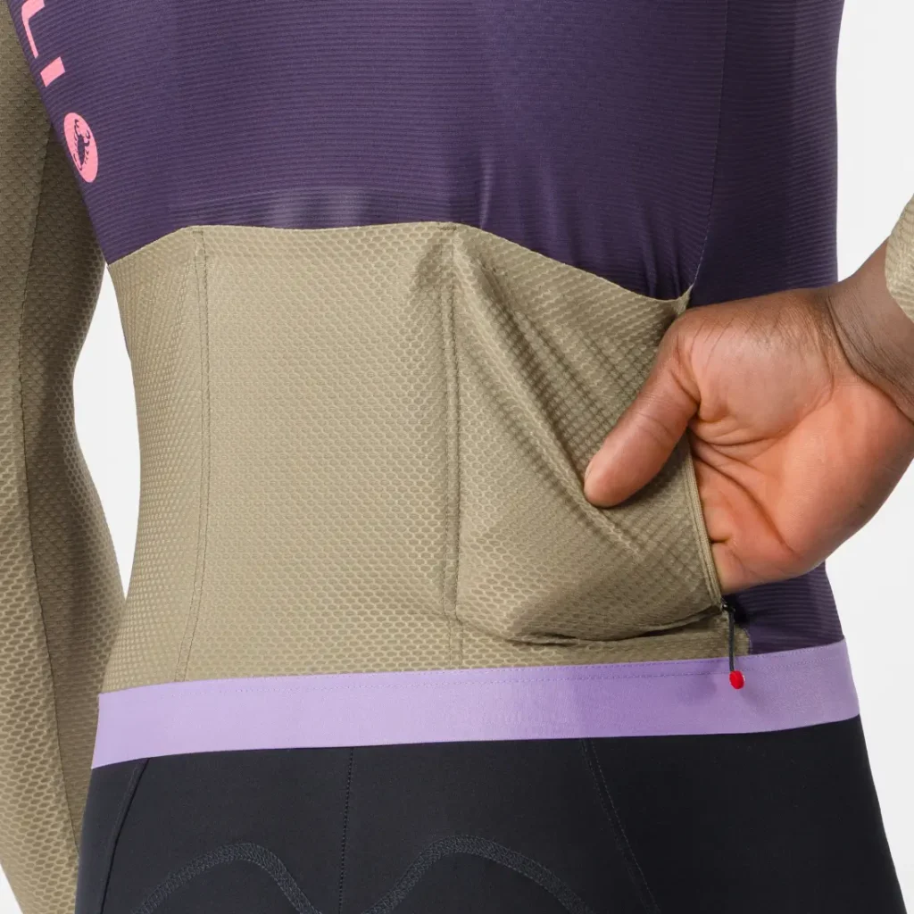 Una persona mete la mano en el bolsillo trasero de un maillot Corretto LS de color beige y morado, mostrando la textura, la elasticidad y el diseño de manga larga del tejido.