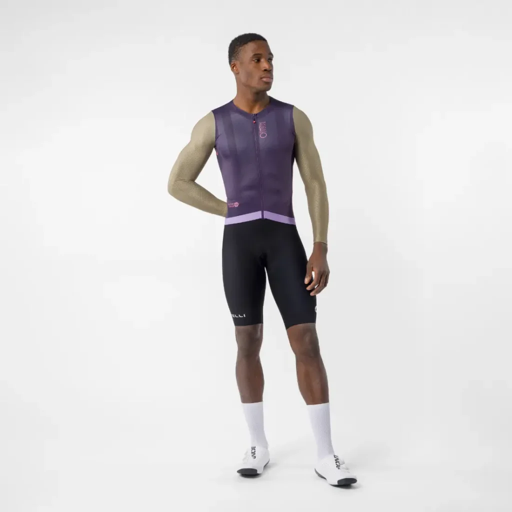 Un hombre posa sobre un fondo blanco con un elegante maillot de ciclismo sin mangas Castelli Transition, que complementa con calcetines blancos y zapatillas de ciclismo; tiene la mano izquierda en la cadera y el brazo derecho relajado a lo largo del cuerpo.
