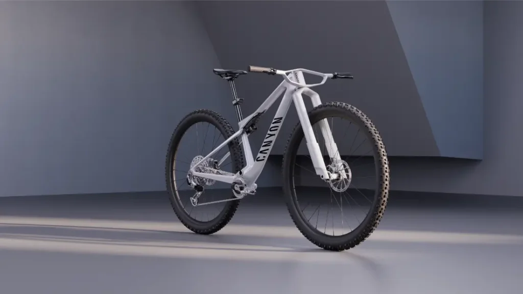 Una moderna bicicleta de montaña Canyon blanca con ruedas de 32″ se expone en un entorno interior minimalista, con paredes grises y un suelo liso.