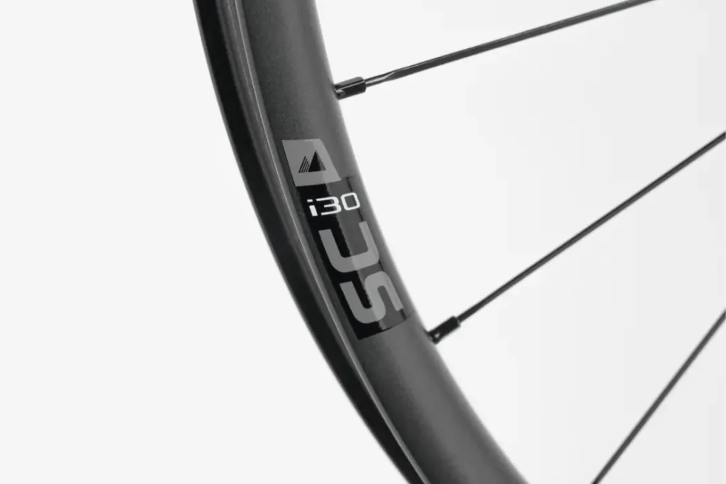 Primer plano de una llanta de bicicleta negra con la etiqueta «i30 SLC» y los radios visibles sobre un fondo blanco liso.