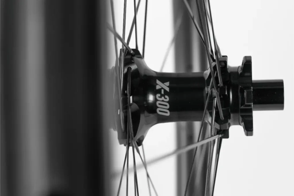 Primer plano de un buje de rueda de bicicleta con la inscripción «X-300» y radios que se extienden radialmente, fotografiado en blanco y negro.