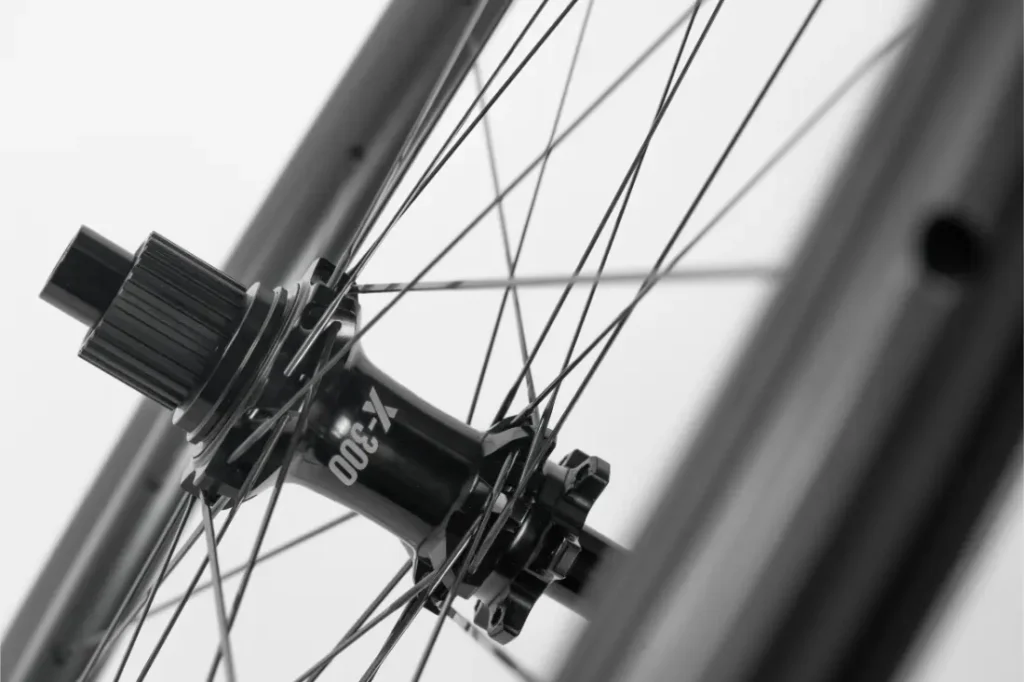 Primer plano en blanco y negro del buje y los radios de una rueda de bicicleta, en el que se aprecian el eje central, las marcas del buje y los radios tensados unidos a la llanta.