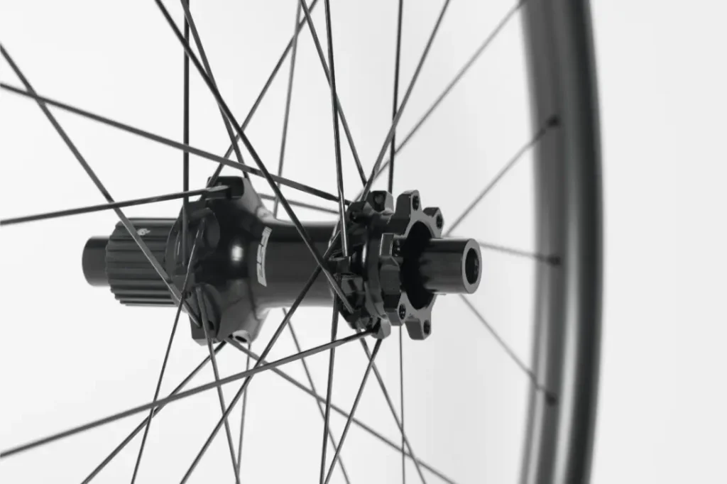 Primer plano de un buje de bicicleta negro con radios que se extienden hacia fuera, sobre un fondo blanco liso.
