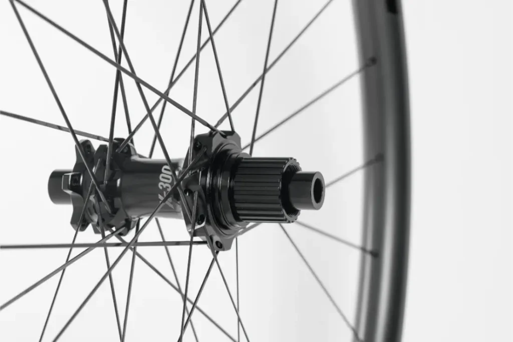 Primer plano de un buje de bicicleta negro con radios que se extienden hacia fuera, sobre un fondo blanco liso.